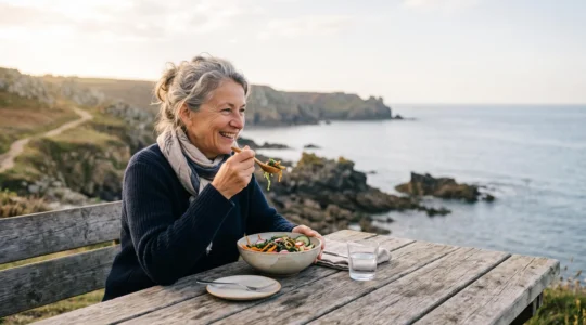 Personne senior savourant un plat à base d'algues marines fraîches face à la mer, symbole d'une alimentation saine après 60 ans